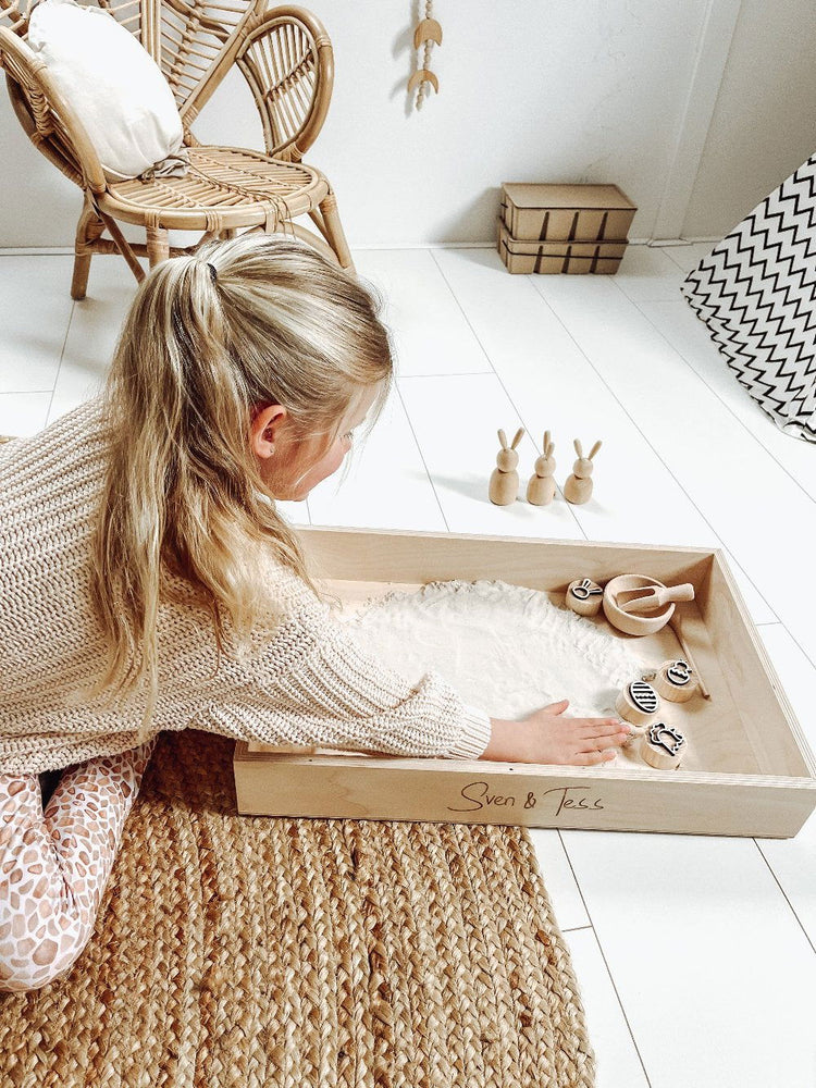 Houten paas stempels - yourlittlefamily-nl - Meisje is aan het spelen in een speelbak met vier houten paasstempels. 